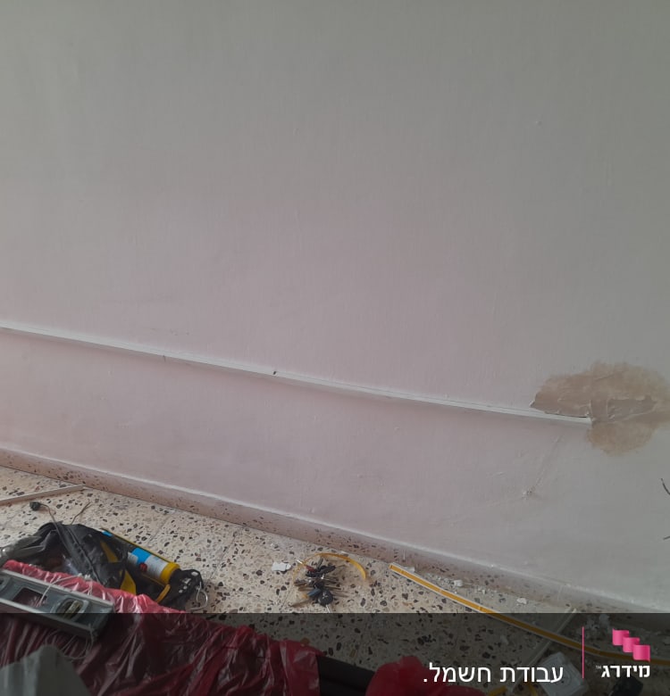 חוטי חשמל יוצאים מקיר, כלי עבודה על הרצפה